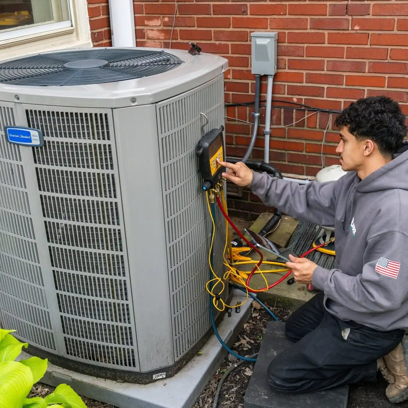 Raber technician taking pressure readings at an American Standard air conditioning condenser beside a brick house, photographed on a Raber job in Northeast Ohio