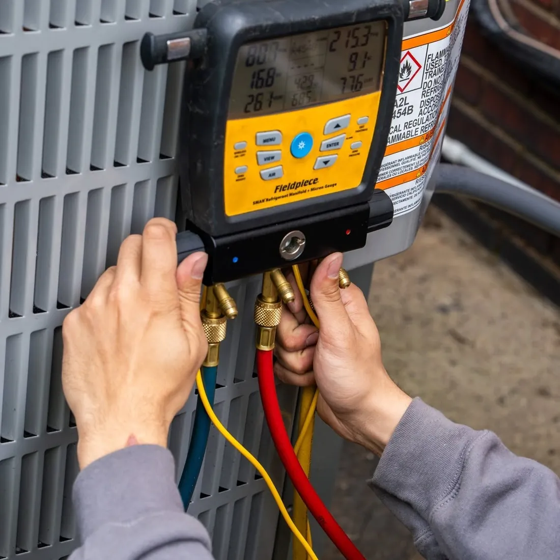 Close up of a digital refrigerant manifold clipped to a condenser with the red, blue and yellow hoses connected, photographed on a Raber job in Northeast Ohio