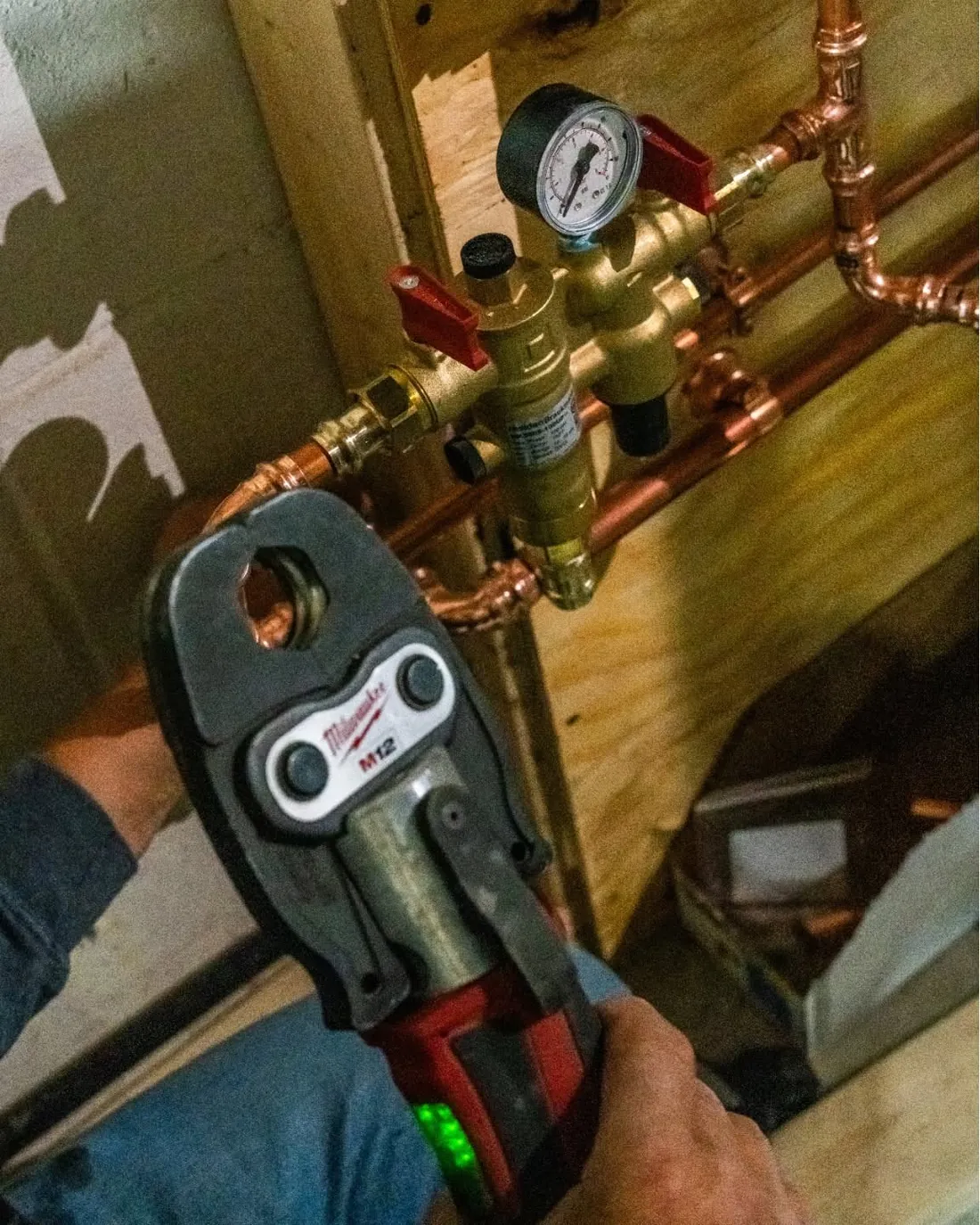 Milwaukee M12 press tool at new copper water piping below a brass valve assembly with a pressure gauge