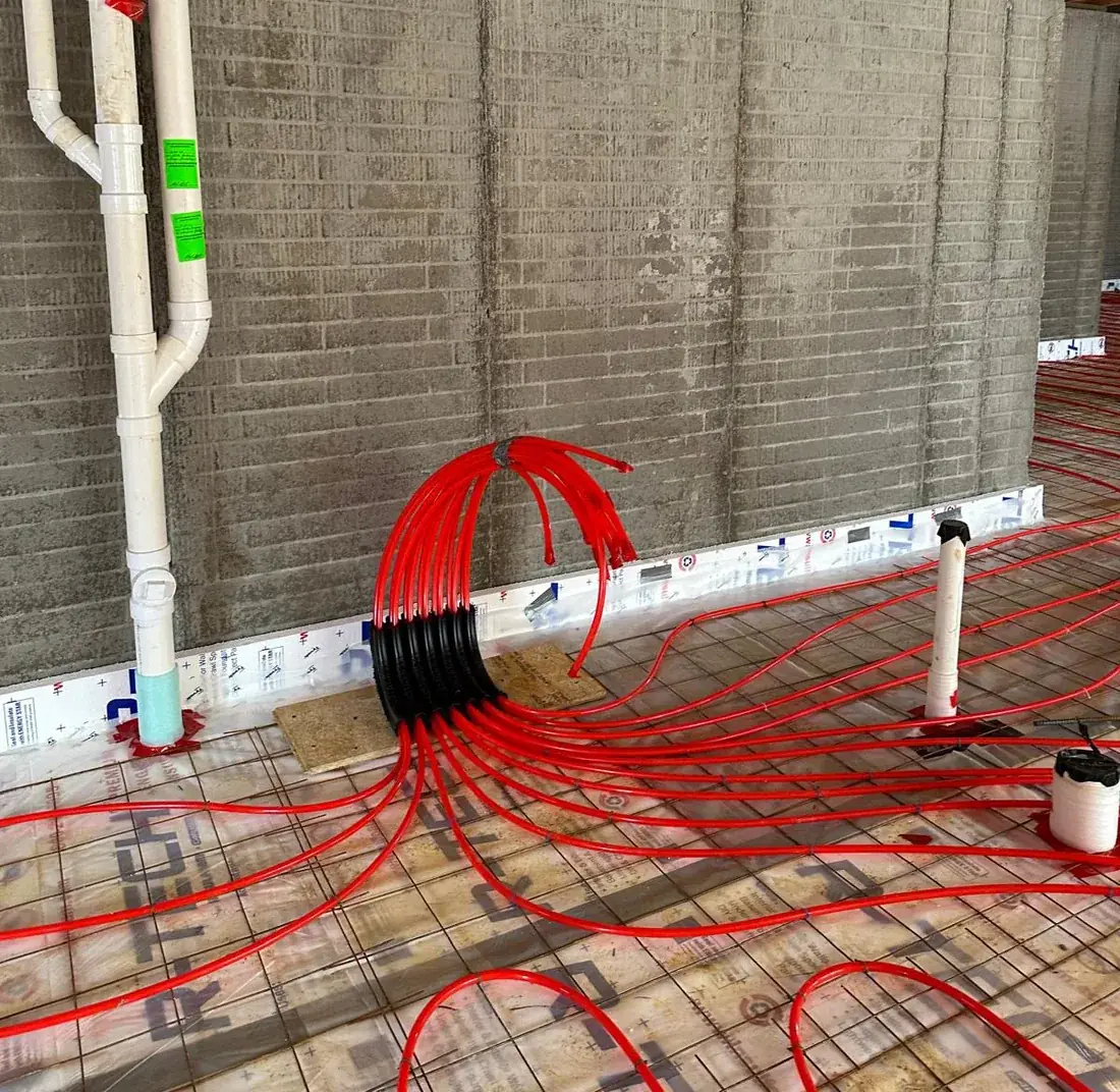 Radiant floor heating PEX tubing tied to reinforcing mesh over a vapor barrier with the manifold stub ready for connection