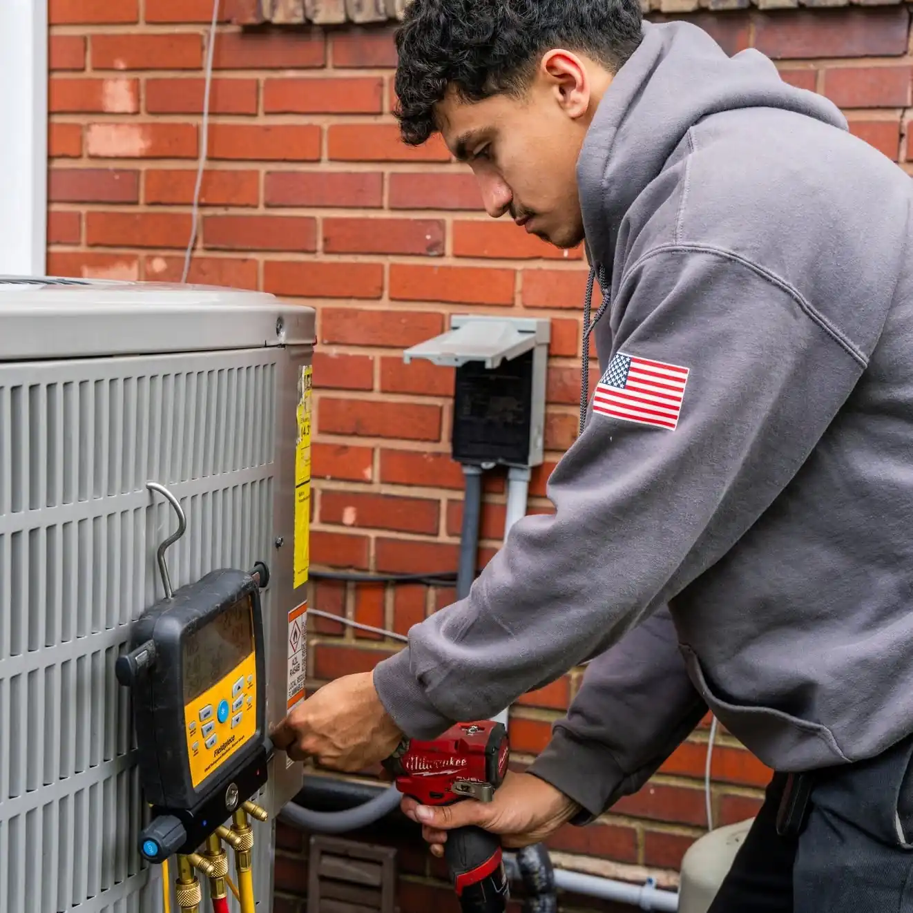 Raber technician working at the service ports of a condenser with a digital manifold hung on the cabinet, photographed on a Raber job in Northeast Ohio