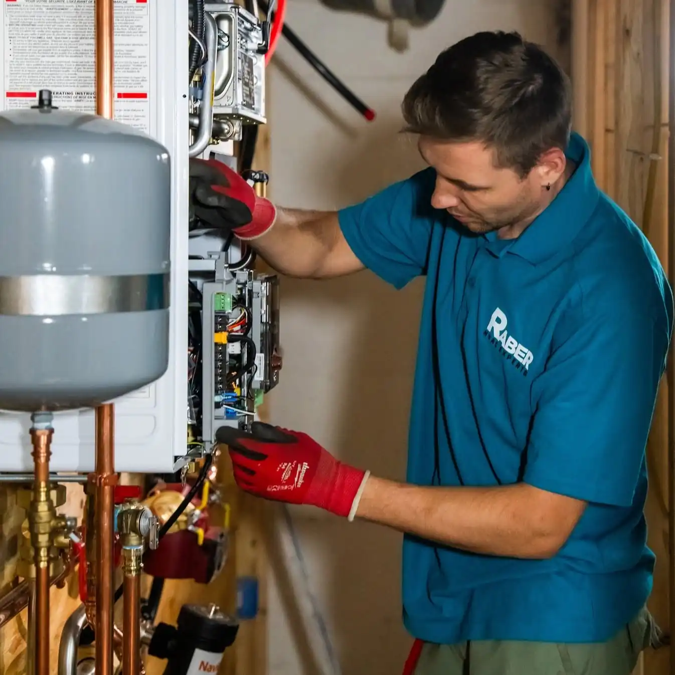 Raber technician working inside the opened control panel of a wall mounted boiler, with the expansion tank alongside