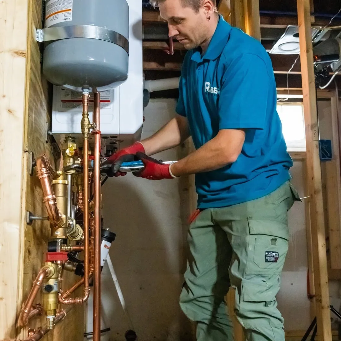 Raber technician press fitting the copper near boiler piping below a wall hung combi boiler, with the expansion tank strapped above it, photographed on a Raber job in Northeast Ohio