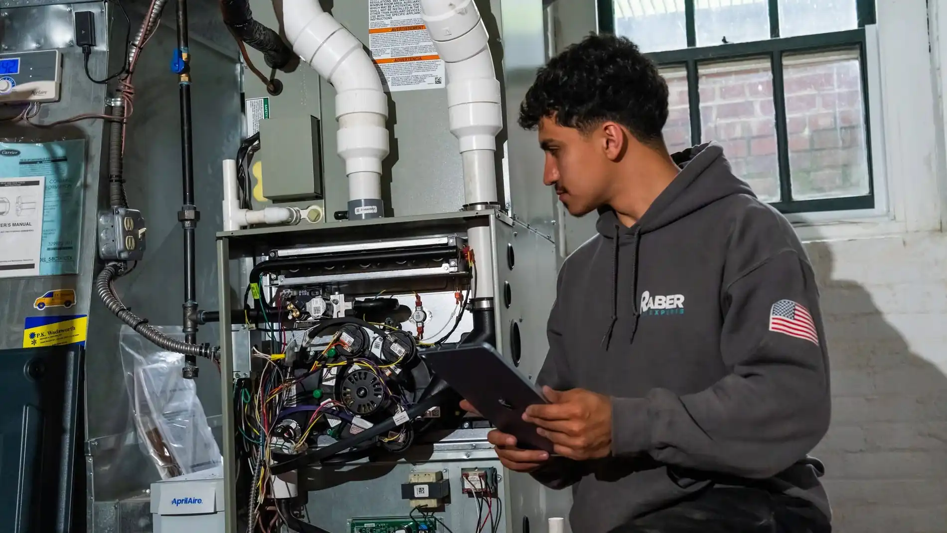 Raber technician reading a tablet in front of an opened furnace with the control board and wiring exposed