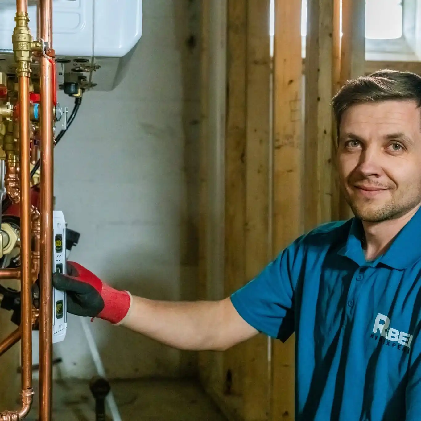Raber technician resting a hand on the copper piping of a wall mounted high efficiency combi boiler in a framed basement, photographed on a Raber job in Northeast Ohio