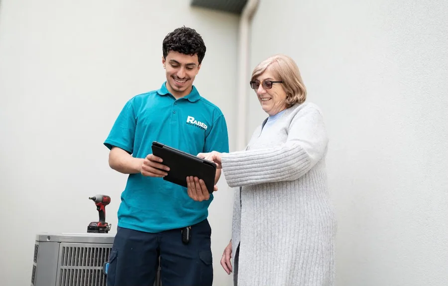 Raber HVAC technician reviewing air conditioning system readings with a homeowner beside her outdoor condenser