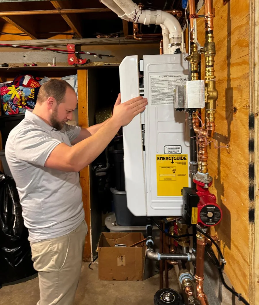 Raber technician servicing a high efficiency wall mounted heating unit with copper piping and a circulator pump
