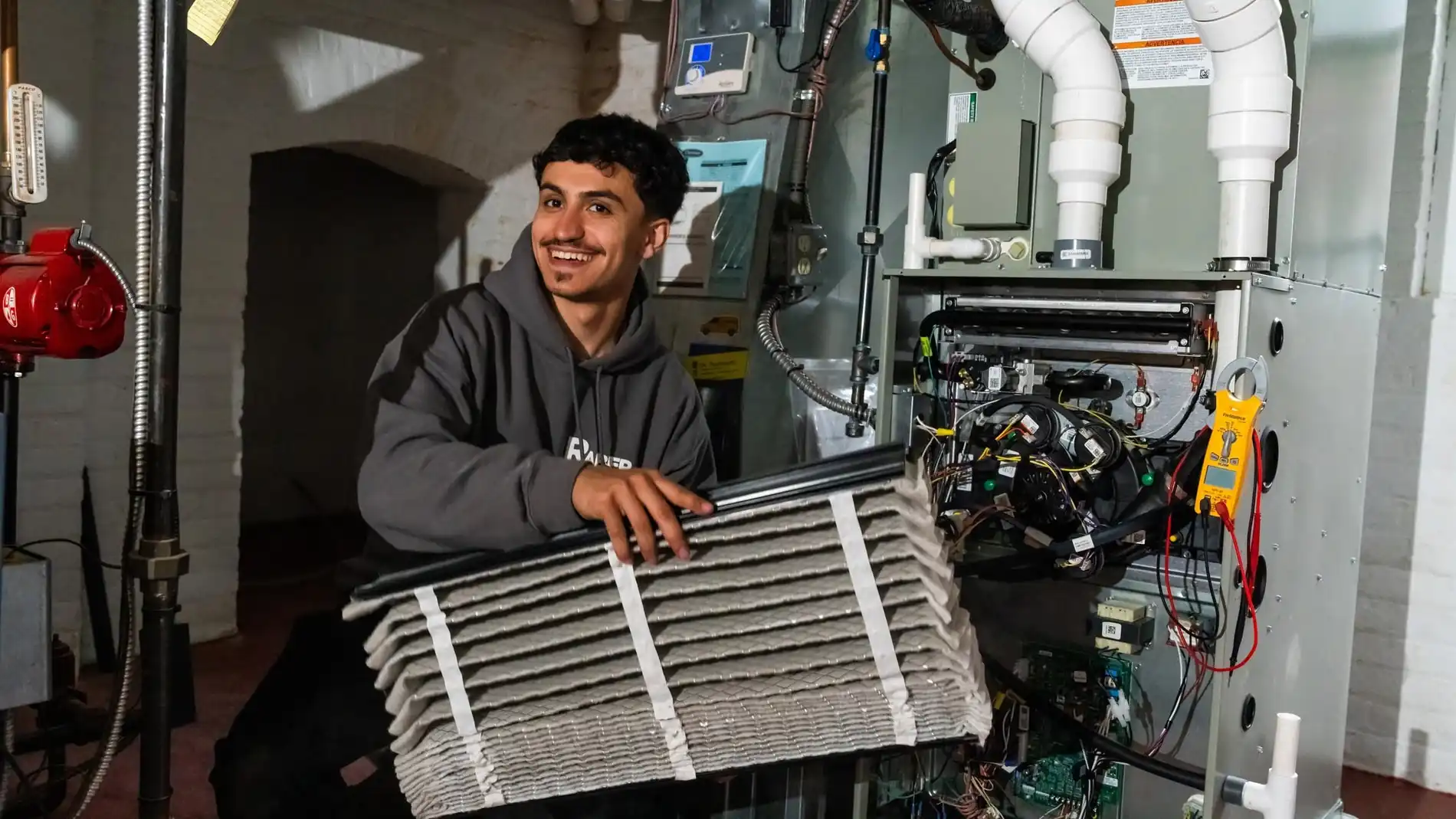 Raber technician holding a used pleated media filter taken out of the opened furnace behind him, photographed on a Raber job in Northeast Ohio