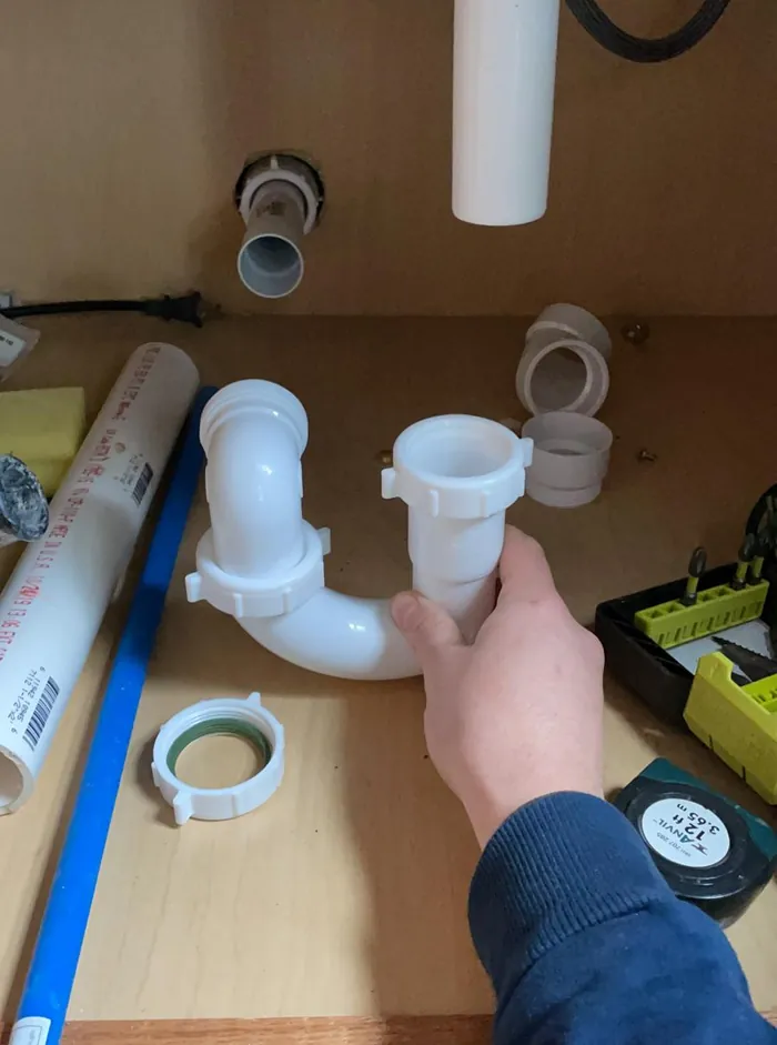 Plumber assembling a new P trap and tailpiece under a kitchen sink during a fixture replacement