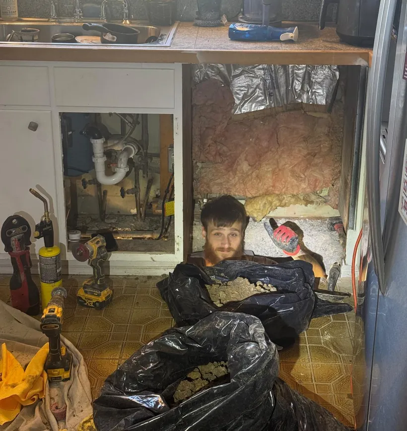 Raber technician working in an opened kitchen floor to replace a failed under slab drain line, with debris bagged alongside
